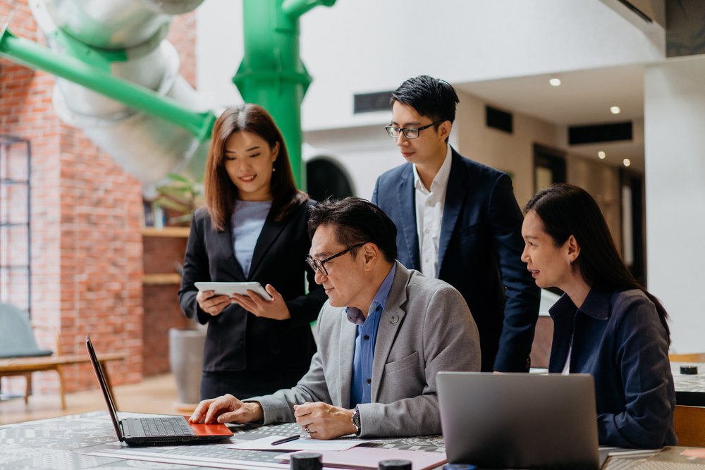 Team leader working at a laptop with three colleagues gathered around, representing managed offshore staffing in the Philippines